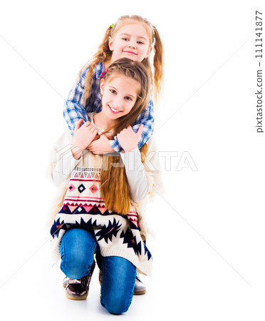 Two little girls sisters in casual clothes posing and hugging each other, isolated on white background 111141877