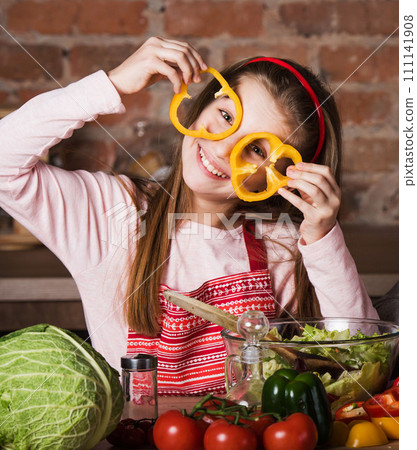 Little chef girl holding slices of pepper before the eyes Little chef girl holding slices of pepper before the eyes 111141908