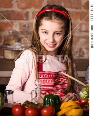 Beautiful little girl in red apron cooking vegetable salad at home 111141910