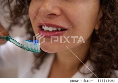 Cropped shot of a young beautiful woman holding toothbrush near her mouth, brushing white healthy teeth in the bathroom. Cropped shot of a young beautiful woman holding toothbrush near her mouth, brushing white healthy teeth in the bathroom. 111141968