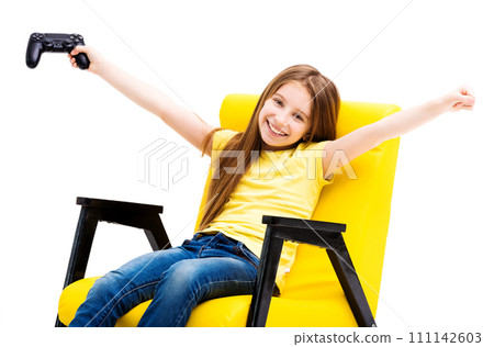 Happy girl in a yellow chair holding up playing console, winning a computer game Happy girl in a yellow chair holding up playing console, winning a computer game 111142603