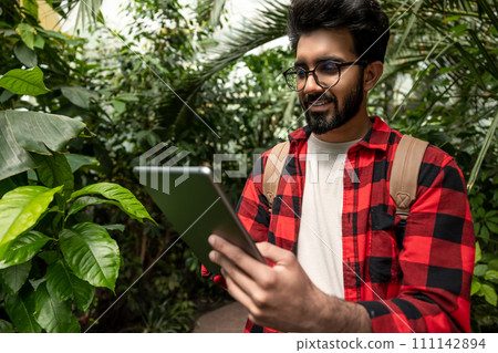 Hindu man with tablet in hands in botanical garden Hindu man with tablet in hands in botanical garden 111142894