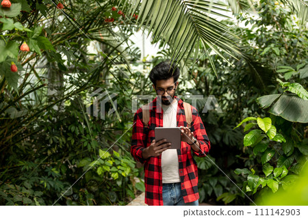 Hindu man with tablet in hands in botanical garden Hindu man with tablet in hands in botanical garden 111142903
