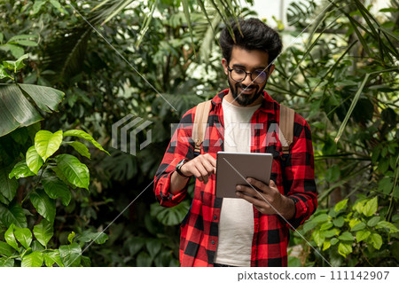 Hindu man with tablet in hands in botanical garden Hindu man with tablet in hands in botanical garden 111142907