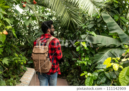 Dark-haired hindu man with backpack walking in botanical garden Dark-haired hindu man with backpack walking in botanical garden 111142909