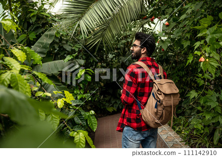 Dark-haired hindu man with backpack walking in botanical garden Dark-haired hindu man with backpack walking in botanical garden 111142910