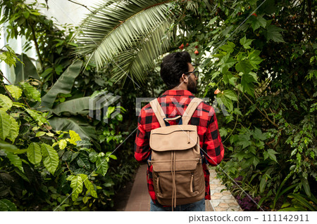 Dark-haired hindu man with backpack walking in botanical garden Dark-haired hindu man with backpack walking in botanical garden 111142911