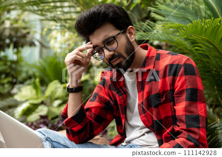 Man in red checkered shirt working on laptop and looking tired Man in red checkered shirt working on laptop and looking tired 111142928