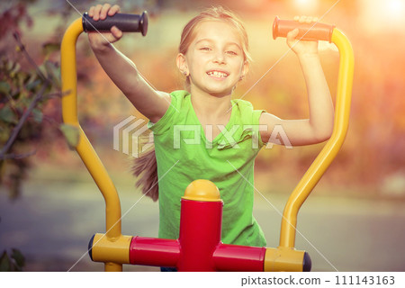 Little girl does exercises at simulator in park Little girl does exercises at simulator in park 111143163