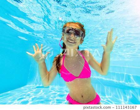 Smiling little girl in swim goggles swimming underwater in pool. Teenage girl diving underwater 111143167