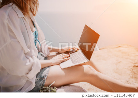 Woman sea laptop. Successful business woman working on laptop by the sea. Pretty lady typing on computer at summer day outdoors. Freelance, digital nomad, travel and holidays concept. Woman sea laptop. Successful business woman working on laptop by the sea. Pretty lady typing on computer at summer day outdoors. Freelance, digital nomad, travel and holidays concept. 111143407