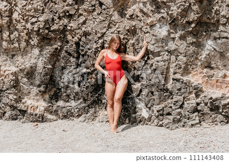 Woman travel portrait. Happy woman with long hair looking at camera and smiling. Close up portrait cute woman in a red bikini posing on a volcanic rock high above the sea Woman travel portrait. Happy woman with long hair looking at camera and smiling. Close up portrait cute woman in a red bikini posing on a volcanic rock high above the sea 111143408