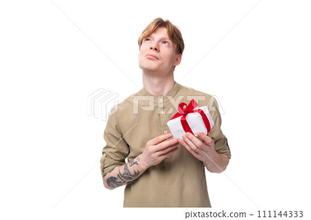 young cute caucasian guy with red hair holding a box with a red ribbon young cute caucasian guy with red hair holding a box with a red ribbon 111144333