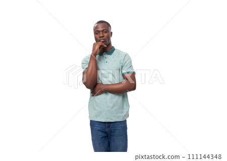 young smart african man dressed in t-shirt and jeans stands holding his chin and thinks young smart african man dressed in t-shirt and jeans stands holding his chin and thinks 111144348