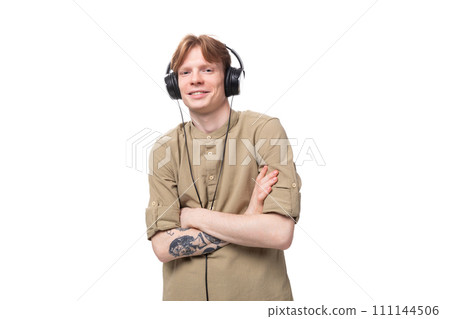 young red-haired guy in glasses and a brown shirt listens to music on headphones 111144506