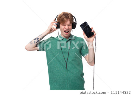 modern stylish energetic young red-haired guy in a green t-shirt listens to music in headphones 111144522