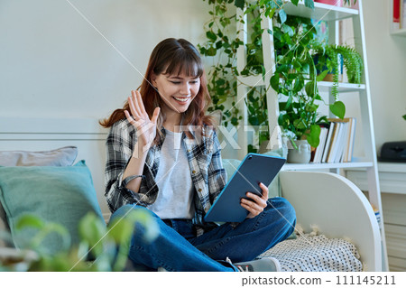 Young smiling female waving hand at digital tablet screen, having video chat with friends Young smiling female waving hand at digital tablet screen, having video chat with friends 111145211
