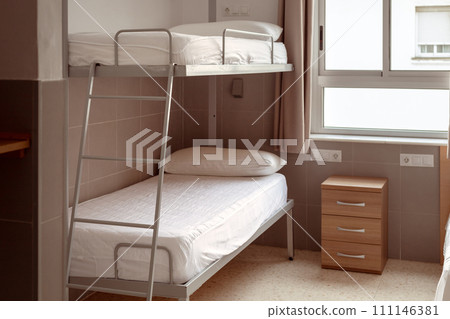 A clean and minimalistic hostel room with a bunk bed, white bedding, and a small wooden bedside table, ideal for budget travelers seeking affordable accommodation. Cheap hostels, save money. 111146381
