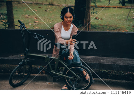 Happy young Asian woman while riding a bicycle in a city park. She smiled using the bicycle of transportation. Environmentally friendly concept. Happy young Asian woman while riding a bicycle in a city park. She smiled using the bicycle of transportation. Environmentally friendly concept. 111146419