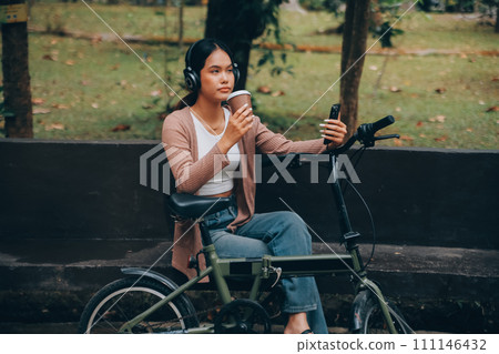 Happy young Asian woman while riding a bicycle in a city park. She smiled using the bicycle of transportation. Environmentally friendly concept. Happy young Asian woman while riding a bicycle in a city park. She smiled using the bicycle of transportation. Environmentally friendly concept. 111146432
