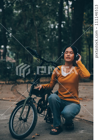 Happy young Asian woman while riding a bicycle in a city park. She smiled using the bicycle of transportation. Environmentally friendly concept. Happy young Asian woman while riding a bicycle in a city park. She smiled using the bicycle of transportation. Environmentally friendly concept. 111146513