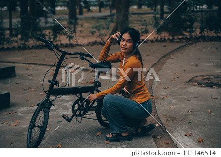 Happy young Asian woman while riding a bicycle in a city park. She smiled using the bicycle of transportation. Environmentally friendly concept. Happy young Asian woman while riding a bicycle in a city park. She smiled using the bicycle of transportation. Environmentally friendly concept. 111146514