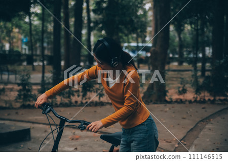 Happy young Asian woman while riding a bicycle in a city park. She smiled using the bicycle of transportation. Environmentally friendly concept. Happy young Asian woman while riding a bicycle in a city park. She smiled using the bicycle of transportation. Environmentally friendly concept. 111146515