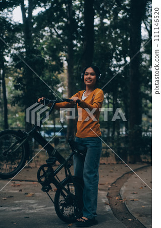 Happy young Asian woman while riding a bicycle in a city park. She smiled using the bicycle of transportation. Environmentally friendly concept. Happy young Asian woman while riding a bicycle in a city park. She smiled using the bicycle of transportation. Environmentally friendly concept. 111146520