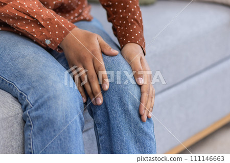 A close-up photo of a body part. African-American young woman's hands hold her leg, she feels severe pain in her knee. A close-up photo of a body part. African-American young woman's hands hold her leg, she feels severe pain in her knee. 111146663