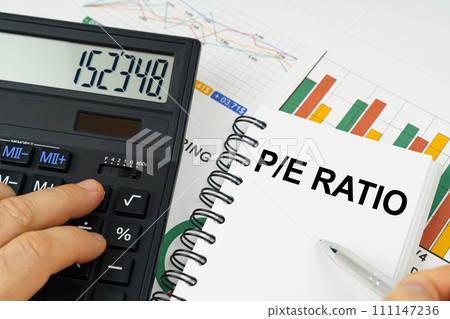 On the table there is a calculator, reports with graphs and a notepad with the inscription - Price-to-Earnings ratio 111147236
