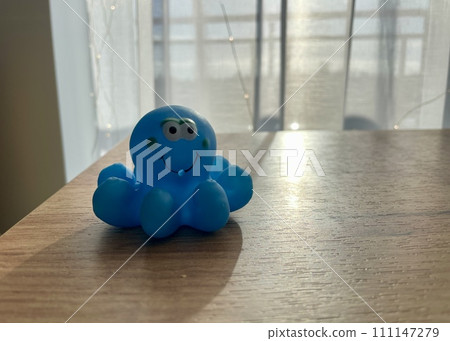 A rubber blue children's toy octopus is illuminated by sunlight in front of the window A rubber blue children's toy octopus is illuminated by sunlight in front of the window 111147279