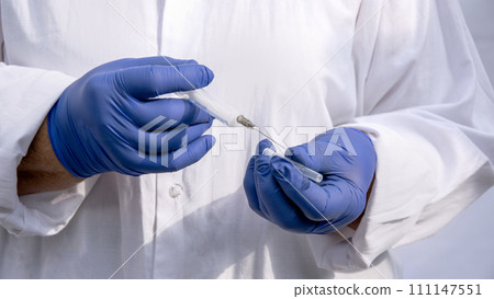 The doctor's hands in blue gloves hold the needle of an injection syringe. The doctor's hands in blue gloves hold the needle of an injection syringe. 111147551