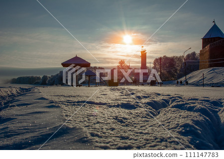 A snow-covered beach with protruding beach umbrellas under a blue sky and a bright sun at sunset 111147783