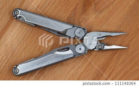 One modern open folding multifunctional knife made of gray iron on a wooden background. Multitool with extended tools and pliers. Compact and portable product. Pocket knife. EDC concept 111148364