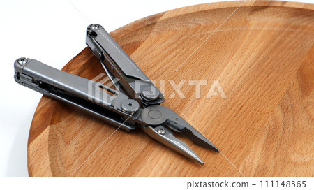 One modern open folding multifunctional knife made of gray iron on a wooden background. Multitool with extended tools and pliers. Compact and portable product. Pocket knife. EDC concept One modern open folding multifunctional knife made of gray iron on a wooden background. Multitool with extended tools and pliers. Compact and portable product. Pocket knife. EDC concept 111148365