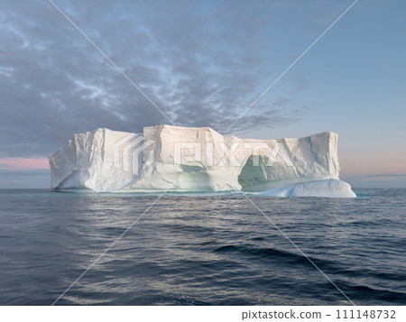 A huge high breakaway glacier drifts in the southern ocean off the coast of Antarctica at sunset, the Antarctic Peninsula, the Southern Arctic Circle, azure water, cloudy weather A huge high breakaway glacier drifts in the southern ocean off the coast of Antarctica at sunset, the Antarctic Peninsula, the Southern Arctic Circle, azure water, cloudy weather 111148732