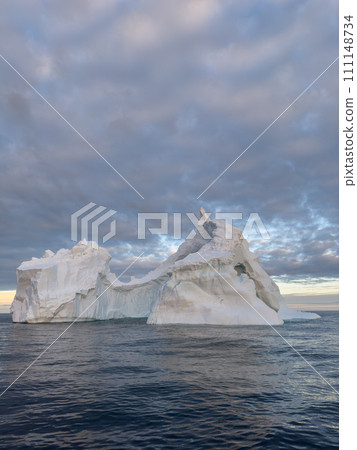 A huge high breakaway glacier drifts in the southern ocean off the coast of Antarctica at sunset, the Antarctic Peninsula, the Southern Arctic Circle, azure water, cloudy weather 111148734