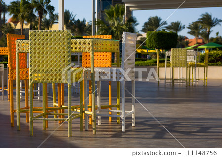 Dining table in a summer outdoor cafe with wicker furniture against the backdrop of an exotic park with palm trees in Egypt Dining table in a summer outdoor cafe with wicker furniture against the backdrop of an exotic park with palm trees in Egypt 111148756