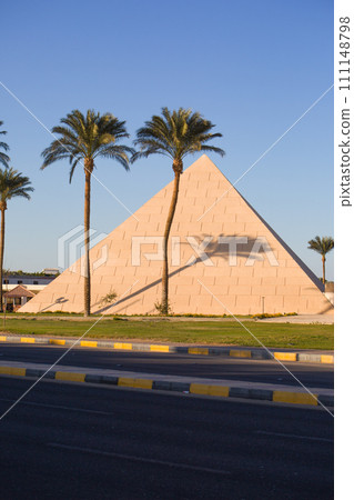 Building in the shape of an Egyptian pyramid with palm trees near the road. Like a great landmark Building in the shape of an Egyptian pyramid with palm trees near the road. Like a great landmark 111148798