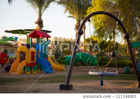 Swing nest on a playground with a sandy floor against the backdrop of exotic palm trees on sunny day 111148801