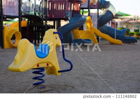 Spring horse made of plastic on a playground for children. Empty space for children to play on the sand outdoors Spring horse made of plastic on a playground for children. Empty space for children to play on the sand outdoors 111148802