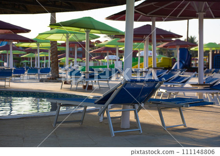 Equipped place to relax under an umbrella by the pool, sun lounger hidden in the shade from the sun on vacation at the hotel Equipped place to relax under an umbrella by the pool, sun lounger hidden in the shade from the sun on vacation at the hotel 111148806