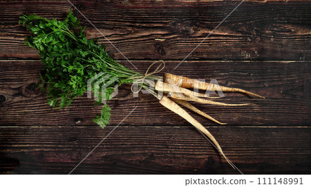 Bunch of parsnip roots with green leaves on rustic dark wooden board, view from above 111148991