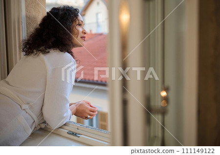 Happy delightful young woman in a white robe looks out the window enjoying the beautiful view of the city of Como 111149122