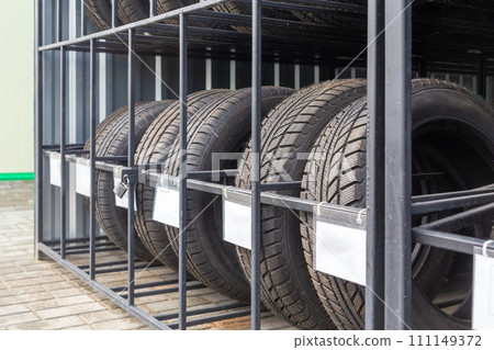 Close-up image of new car tires arranged on metal shelving in outdoors shop. 111149372