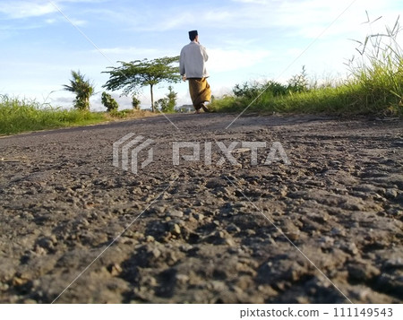 Muslim man walking on a rural asphalt road wearing Islamic cultural clothing from the South Asian region 111149543