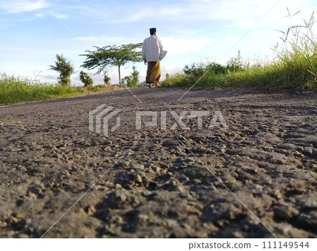 Muslim man walking on a rural asphalt road wearing Islamic cultural clothing from the South Asian region 111149544
