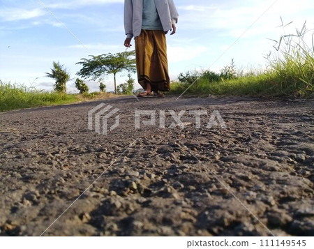 Muslim man walking on a rural asphalt road wearing Islamic cultural clothing from the South Asian region Muslim man walking on a rural asphalt road wearing Islamic cultural clothing from the South Asian region 111149545