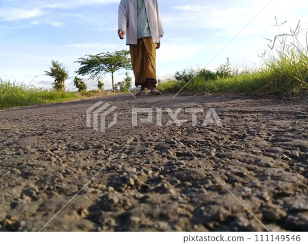 Muslim man walking on a rural asphalt road wearing Islamic cultural clothing from the South Asian region 111149546