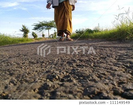 Muslim man walking on a rural asphalt road wearing Islamic cultural clothing from the South Asian region Muslim man walking on a rural asphalt road wearing Islamic cultural clothing from the South Asian region 111149549